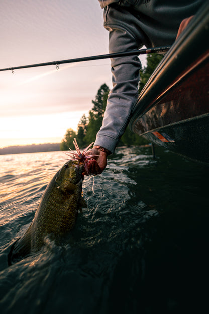 Person holding a fish caught from a kayak on a lake at sunset.